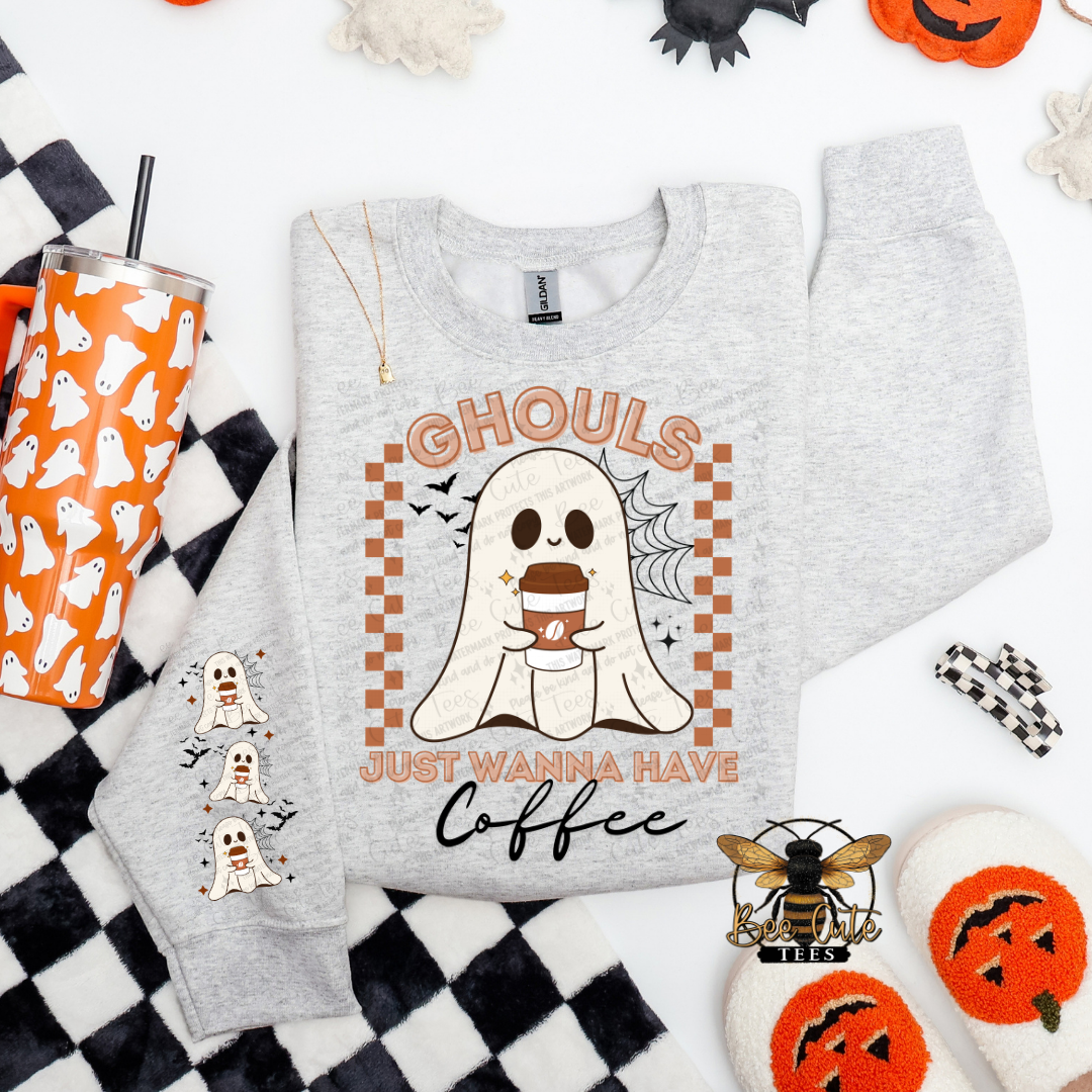 A light heather gray sweatshirt laid flat on a white background with Halloween-themed props. The sweatshirt features a ghost graphic holding a coffee cup, with the text 'GHOULS JUST WANNA HAVE Coffee' and small ghost illustrations on the sleeve.