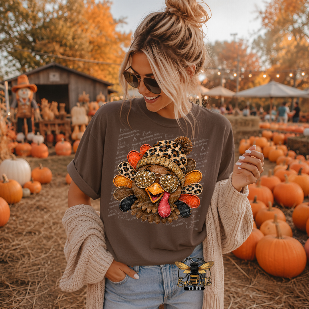 A woman wearing a brown graphic t-shirt with a turkey design and a beige cardigan, standing in a pumpkin patch.