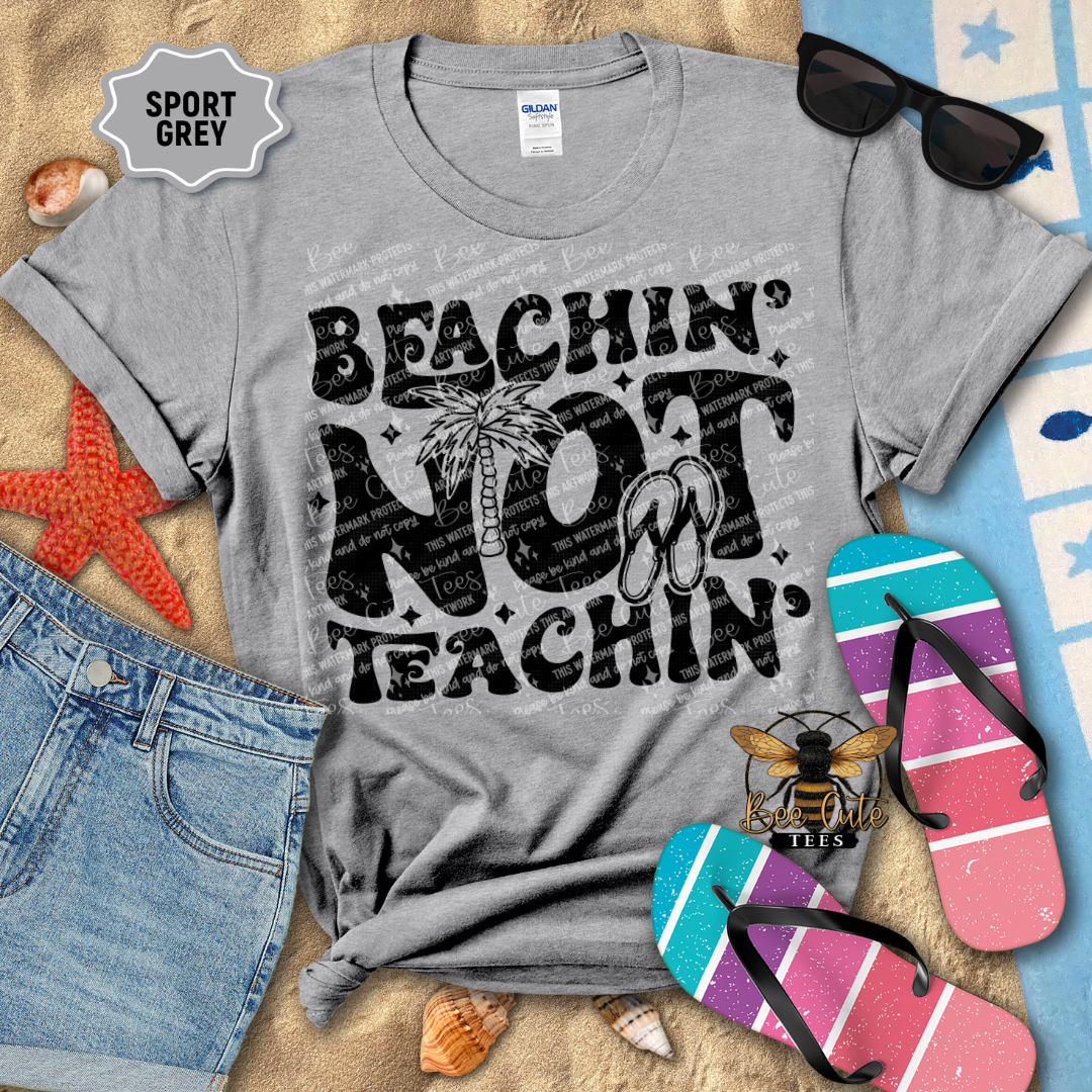 Gray t-shirt with 'Beachin' Not Teachin' design on a beach-themed background with sunglasses, flip-flops, and starfish.