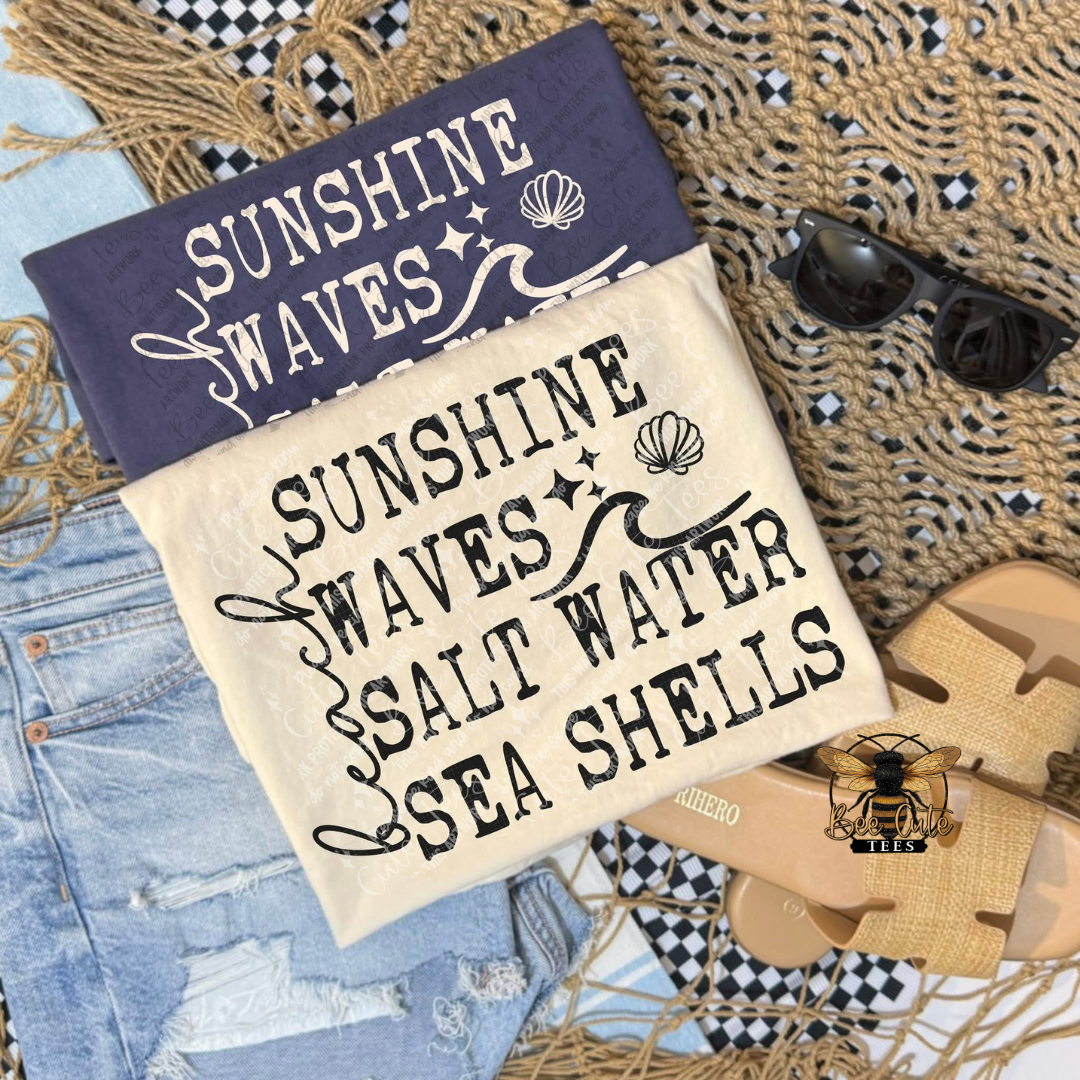 Two t-shirts with 'Sunshine Waves Salt Water Sea Shells' text on a textured surface.