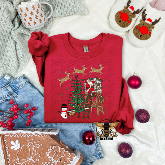 Red Christmas-themed sweatshirt with Santa and reindeer design, surrounded by festive items on a white surface.