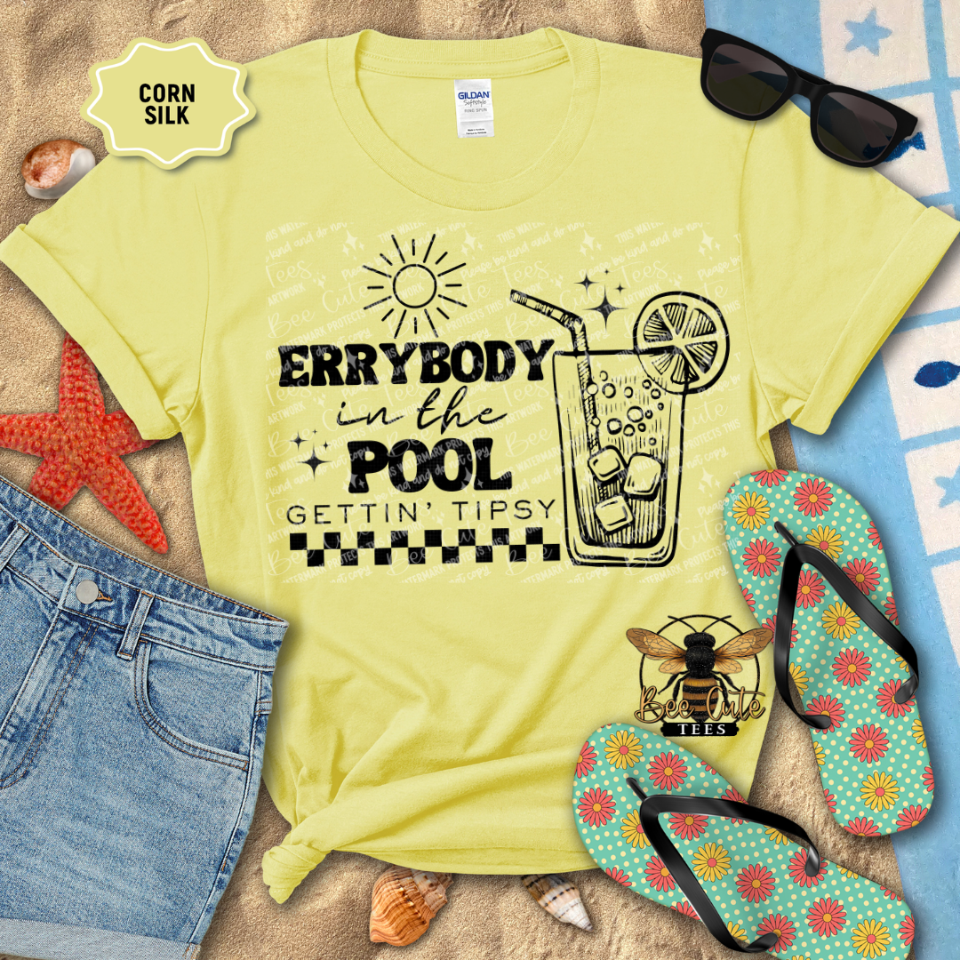 Yellow t-shirt with a pool-themed design on a beach setting with sunglasses, flip-flops, and jeans.