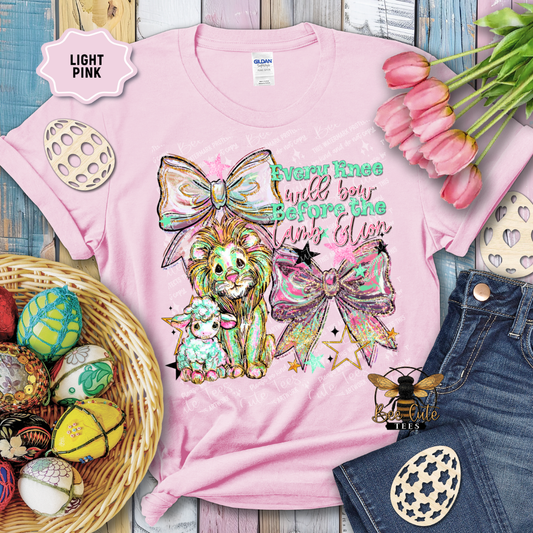 Pink t-shirt with a colorful design featuring a lion, sheep, and decorative elements on a wooden surface with Easter decorations.