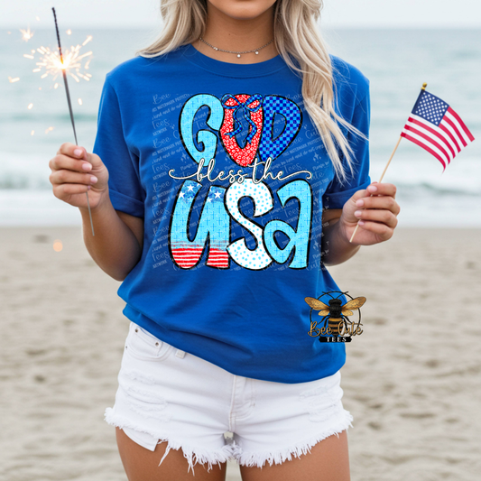 Person wearing a blue t-shirt with 'God Bless the USA' text on a beach.