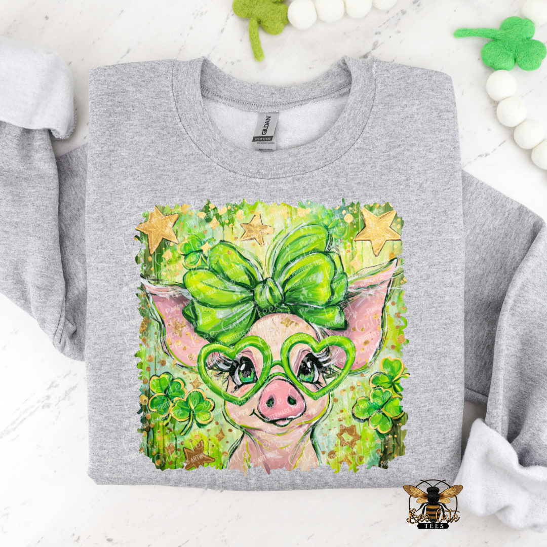 Gray sweatshirt with a colorful design of a pig wearing green glasses and a bow, surrounded by shamrocks on a white background.