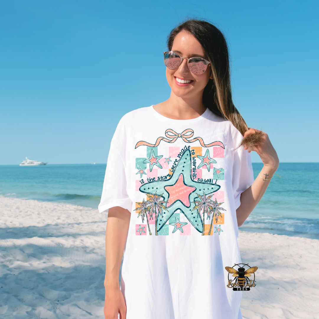 Woman wearing a white t-shirt with a colorful starfish design on a beach.