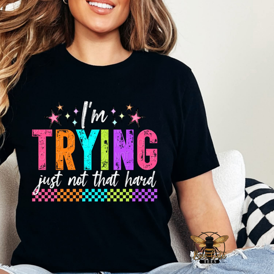 Person wearing a black t-shirt with colorful text 'I'm TRYING just not that hard' on a light background.