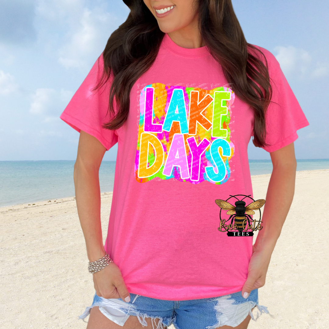 Person wearing a pink 'Lake Days' t-shirt on a beach