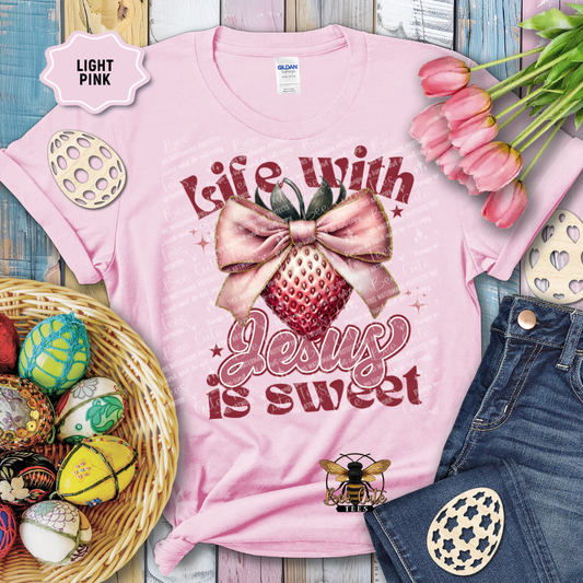Light pink t-shirt with 'Life with Jesus is sweet' design, surrounded by Easter decorations on a wooden surface.