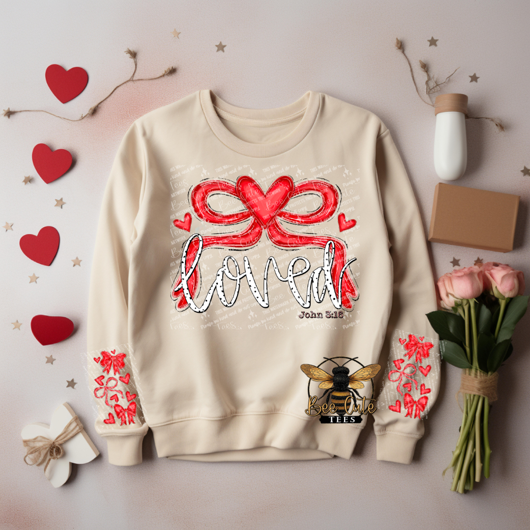Beige sweatshirt with red bow and 'loved' text, surrounded by decorative items on a light background