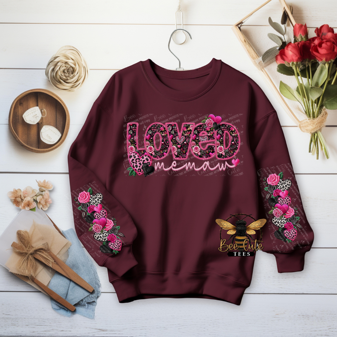 Maroon sweatshirt with floral designs and text on a wooden surface with decorative items.