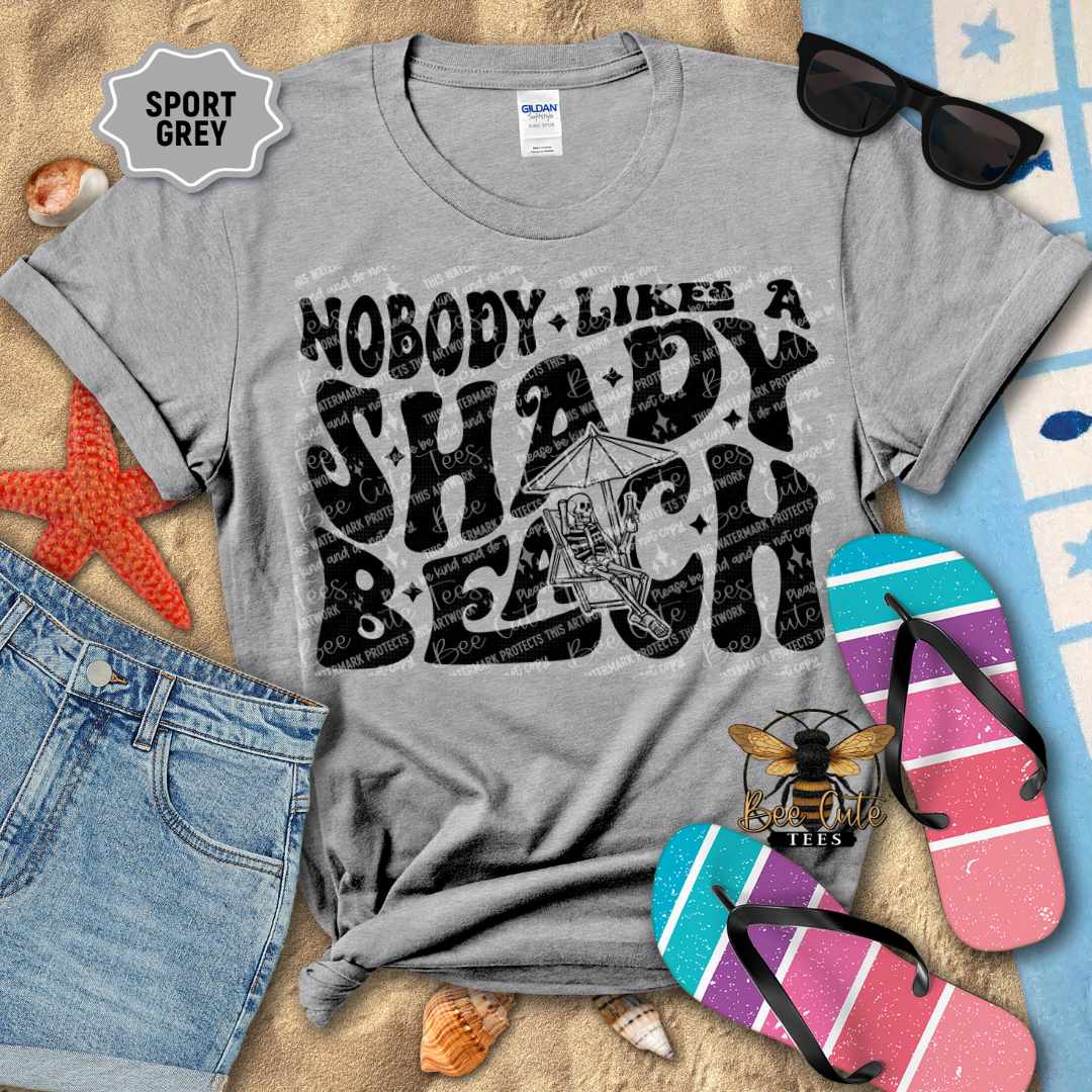 Gray t-shirt with 'Nobody Likes a Shady Beach' text, sunglasses, and flip-flops on a beach-themed background.