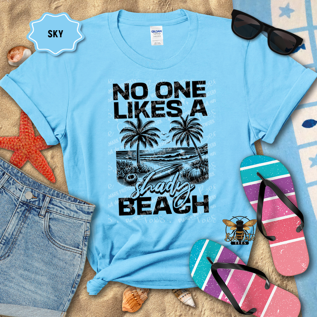 Light blue t-shirt with beach graphic and text, sunglasses, flip-flops, and denim shorts on a sandy background.