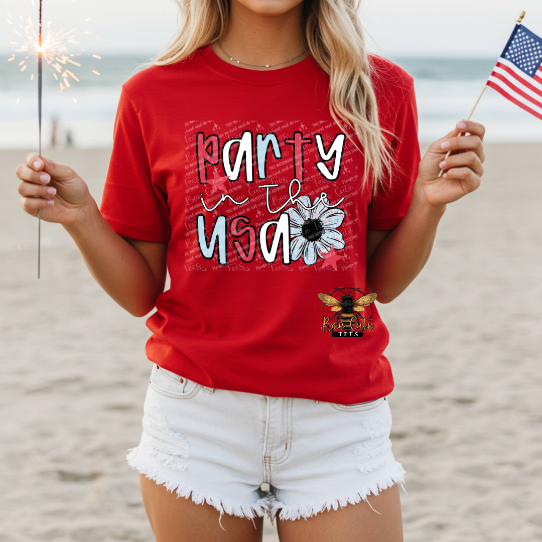 Person wearing a red t-shirt with 'Party in the USA' text on a beach