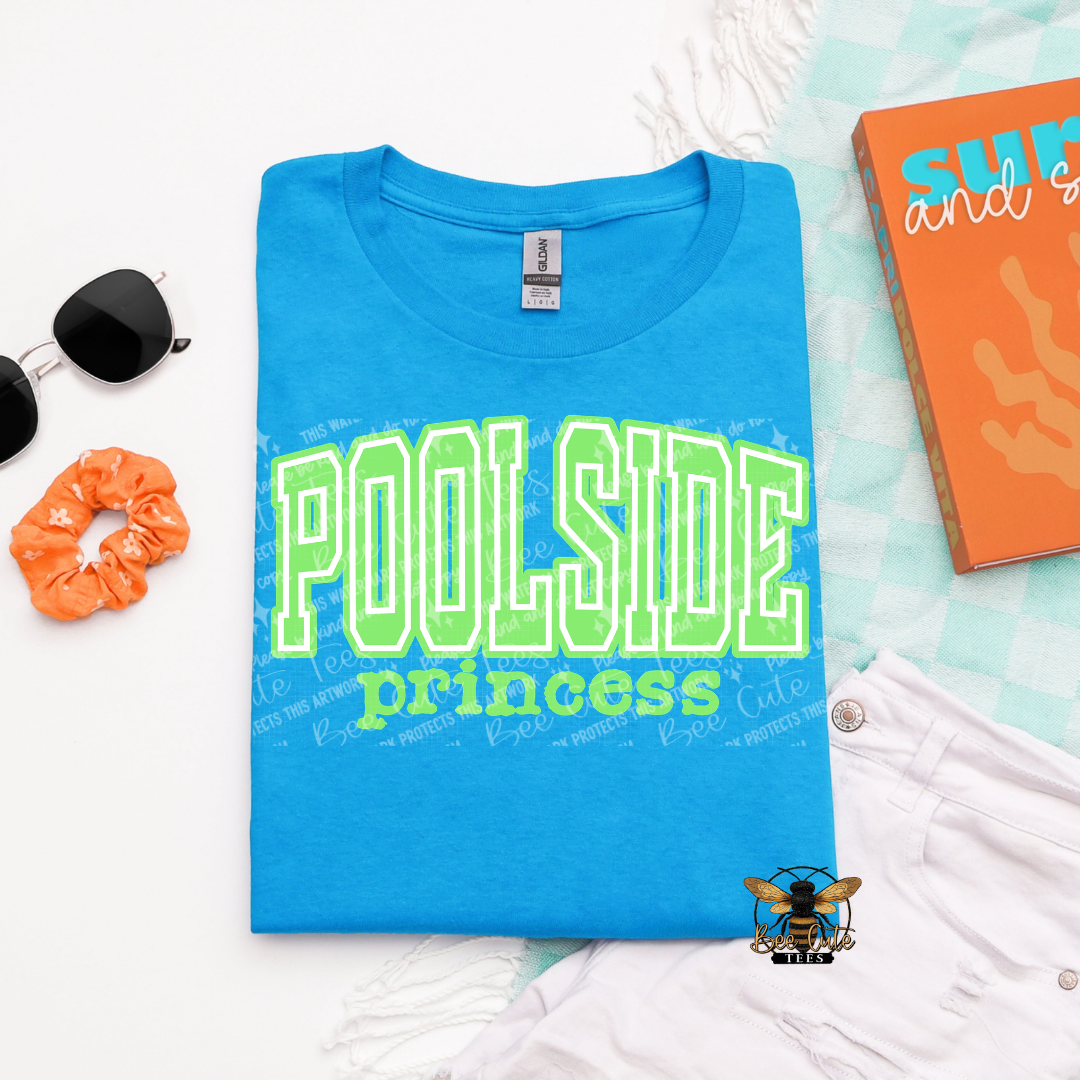 Blue t-shirt with 'Poolside princess' text on a white surface with accessories.