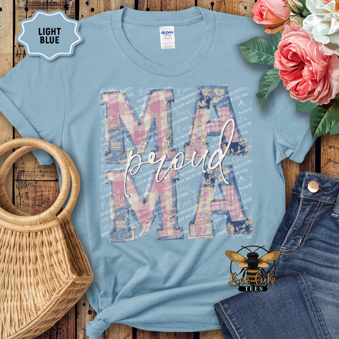 Light blue t-shirt with 'Proud Mama' design on a wooden surface with flowers and denim jeans.