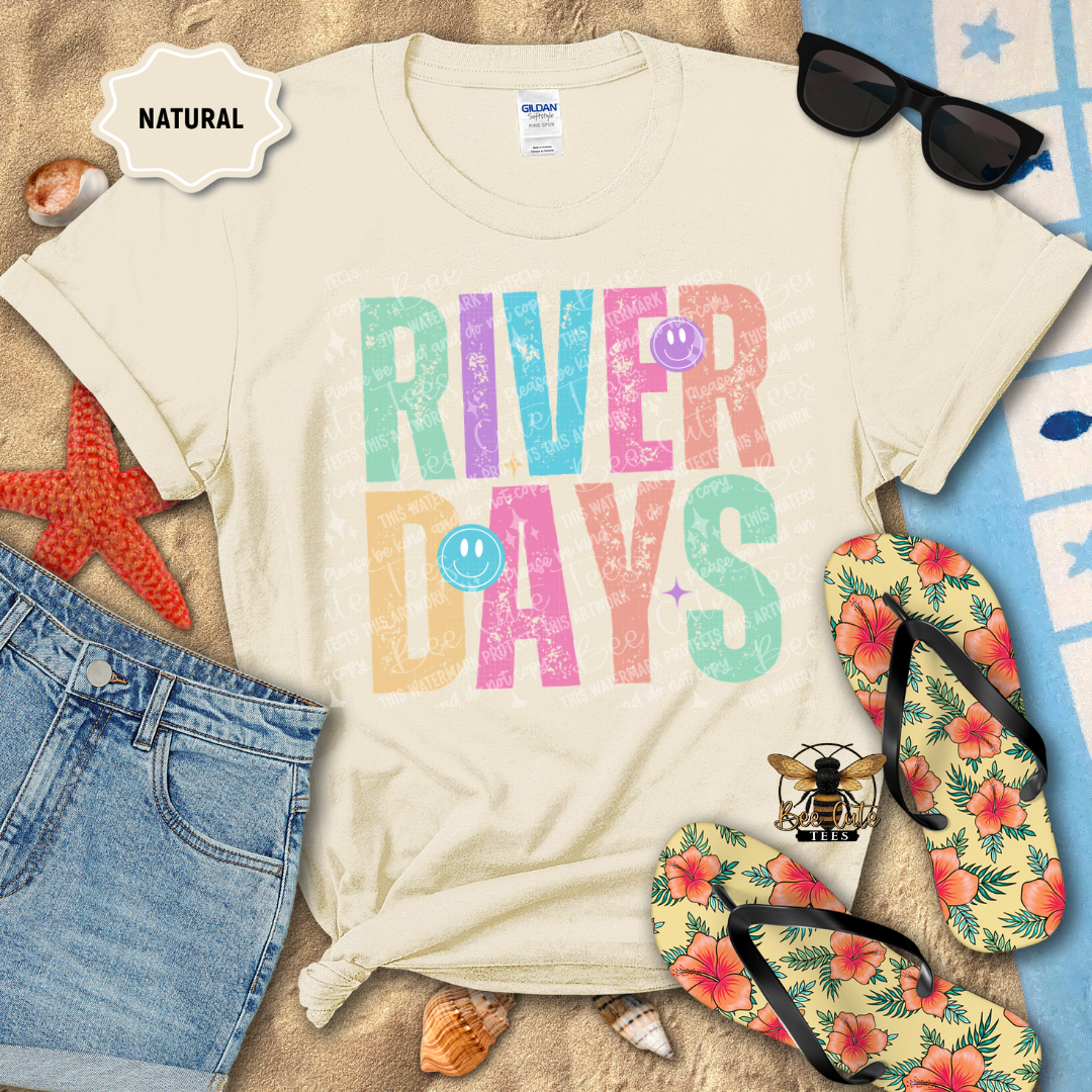 Beige t-shirt with 'River Days' text, sunglasses, flip-flops, and beach items on a sandy background