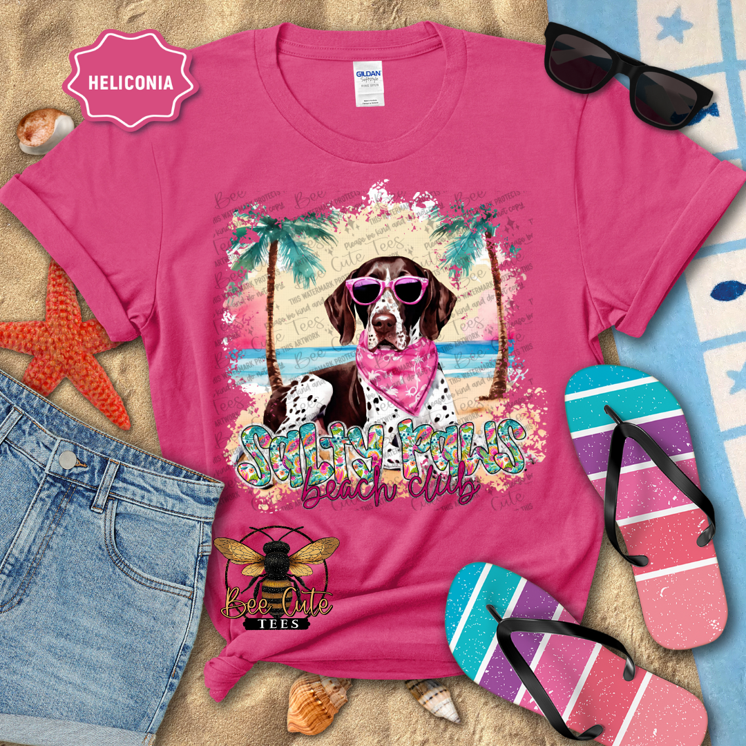 Pink t-shirt with a dog graphic and 'Beach Club' text, surrounded by beach accessories.