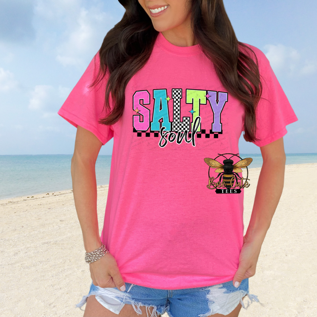 Person wearing a pink t-shirt with 'Salty Soul' design on a beach