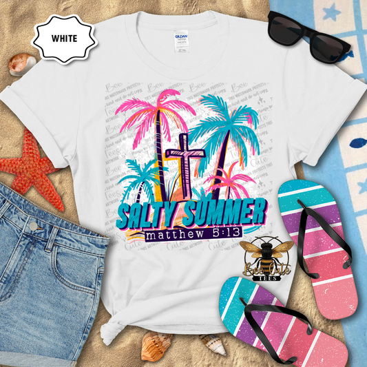 White t-shirt with 'Salty Summer' design, sunglasses, flip-flops, and beach accessories on a sandy background.