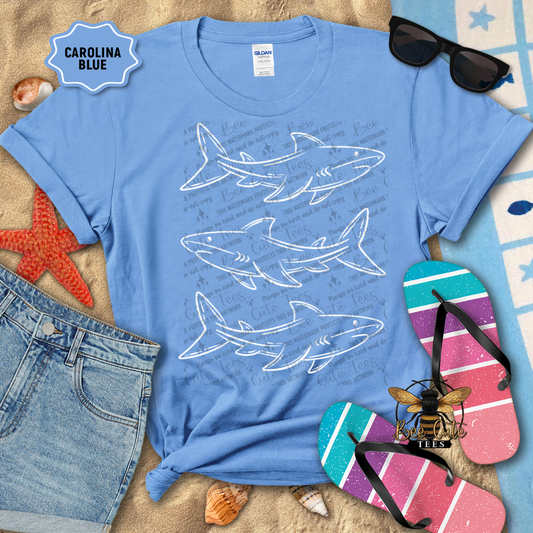 Blue t-shirt with shark designs on a sandy background with beach accessories.