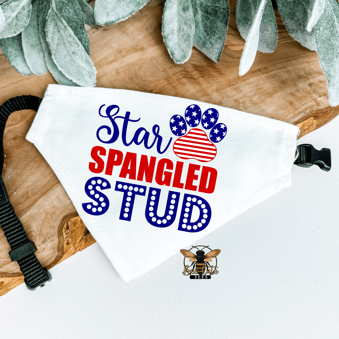 Dog bandana with 'Star Spangled Stud' text on a wooden surface with greenery.