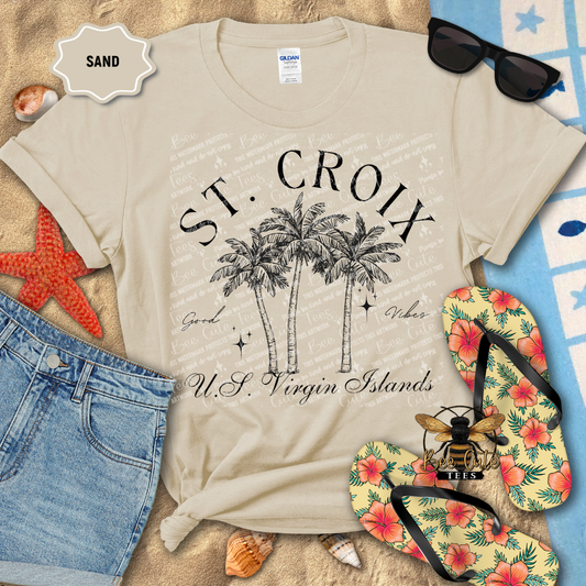 Beige t-shirt with 'St. Croix U.S. Virgin Islands' design on a sandy background with flip-flops and sunglasses.