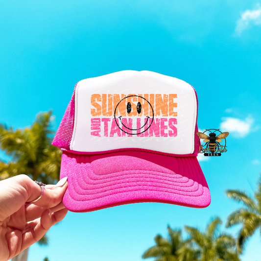 Pink and white cap with 'Sunshine and Tanlines' text against a blue sky background