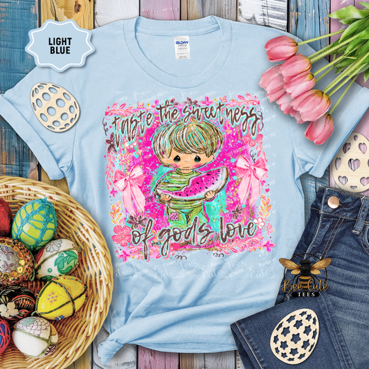 Light blue t-shirt with colorful graphic design featuring a child holding watermelon, surrounded by Easter eggs and tulips.
