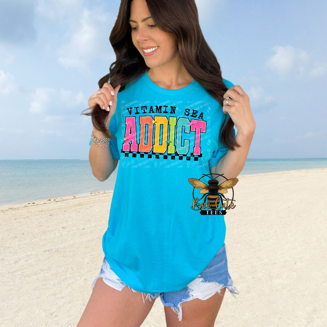 Woman wearing a blue t-shirt with 'Vitamin Sea Addict' text on a beach