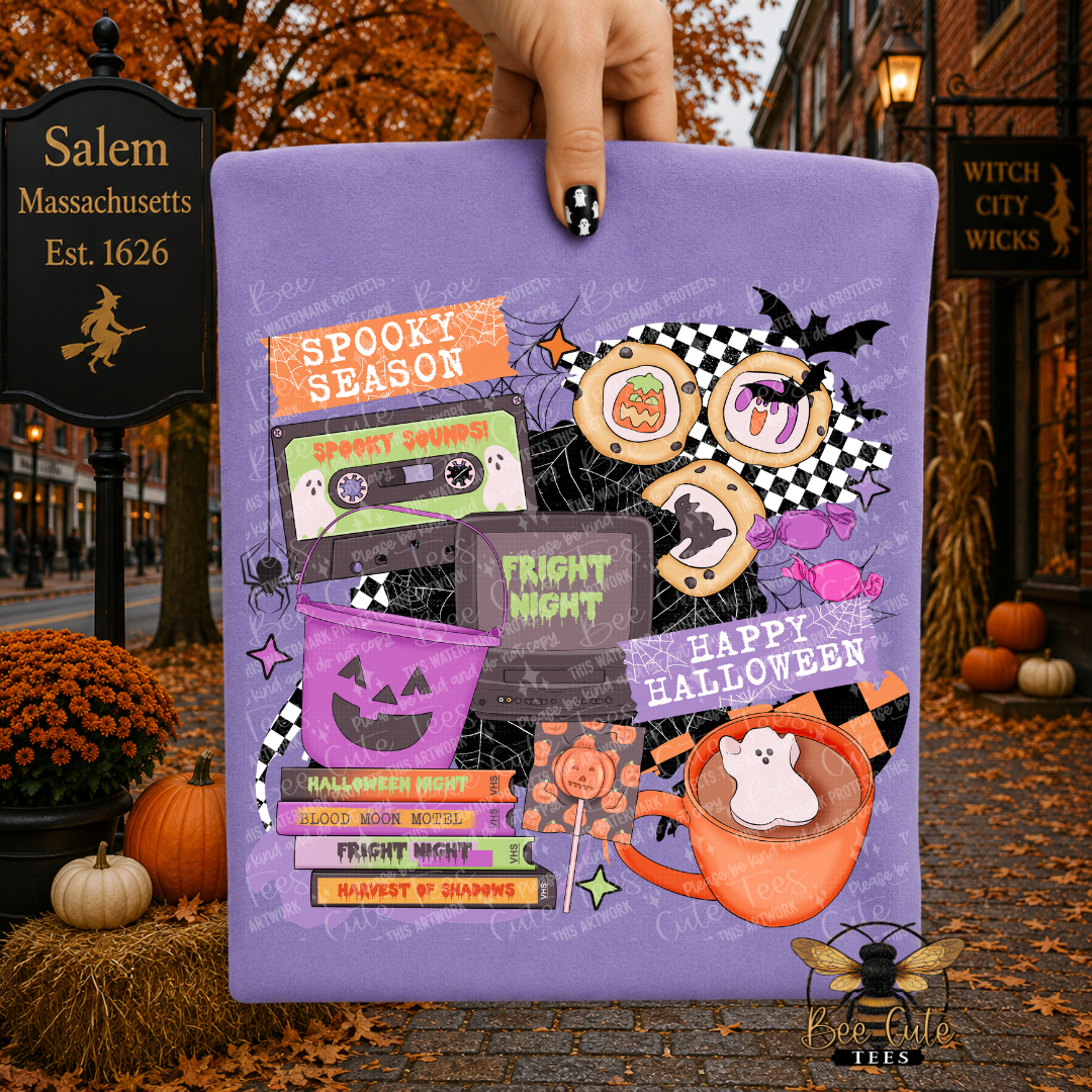 A hand holds a purple folded t-shirt graphic print featuring Halloween-themed illustrations and text, including 'SPOOKY SEASON,' 'FRIGHT NIGHT,' 'HAPPY HALLOWEEN,' a jack-o'-lantern, an orange mug with a ghost, and spooky props. The background is a Halloween street scene with pumpkins, fall leaves, and signs reading Salem, Massachusetts and Witch City Wicks.