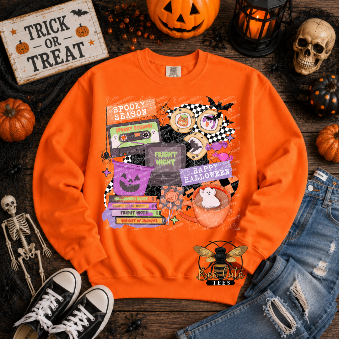 An orange crewneck sweatshirt with a colorful Halloween-themed graphic print, styled in a flat-lay arrangement with jeans, sneakers, a skull, pumpkins, and a 'Trick or Treat' sign on a dark wooden background.