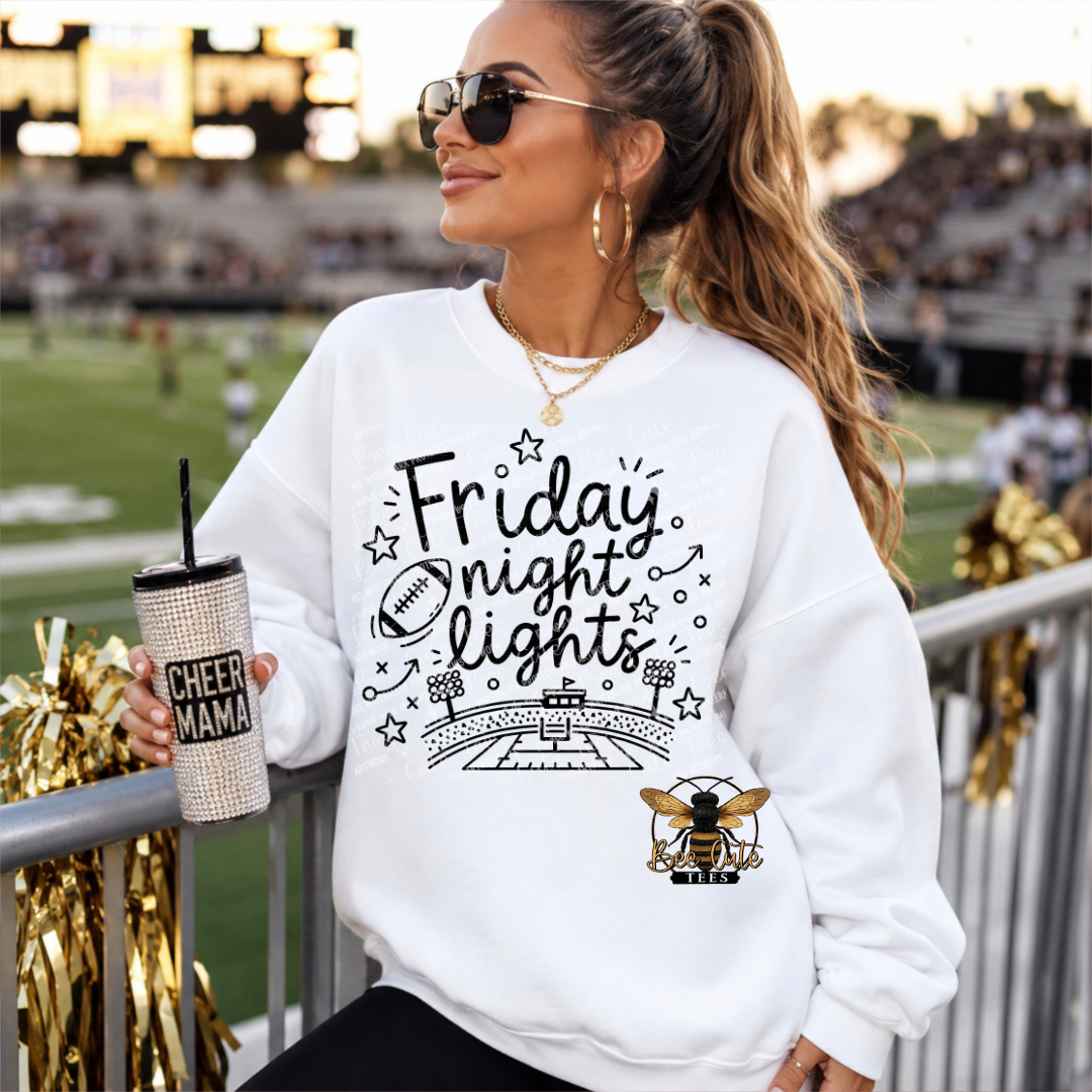 A woman wearing a white graphic sweatshirt with 'Friday Night Lights' and a bee logo, sitting at a stadium railing and holding a glittery tumbler.