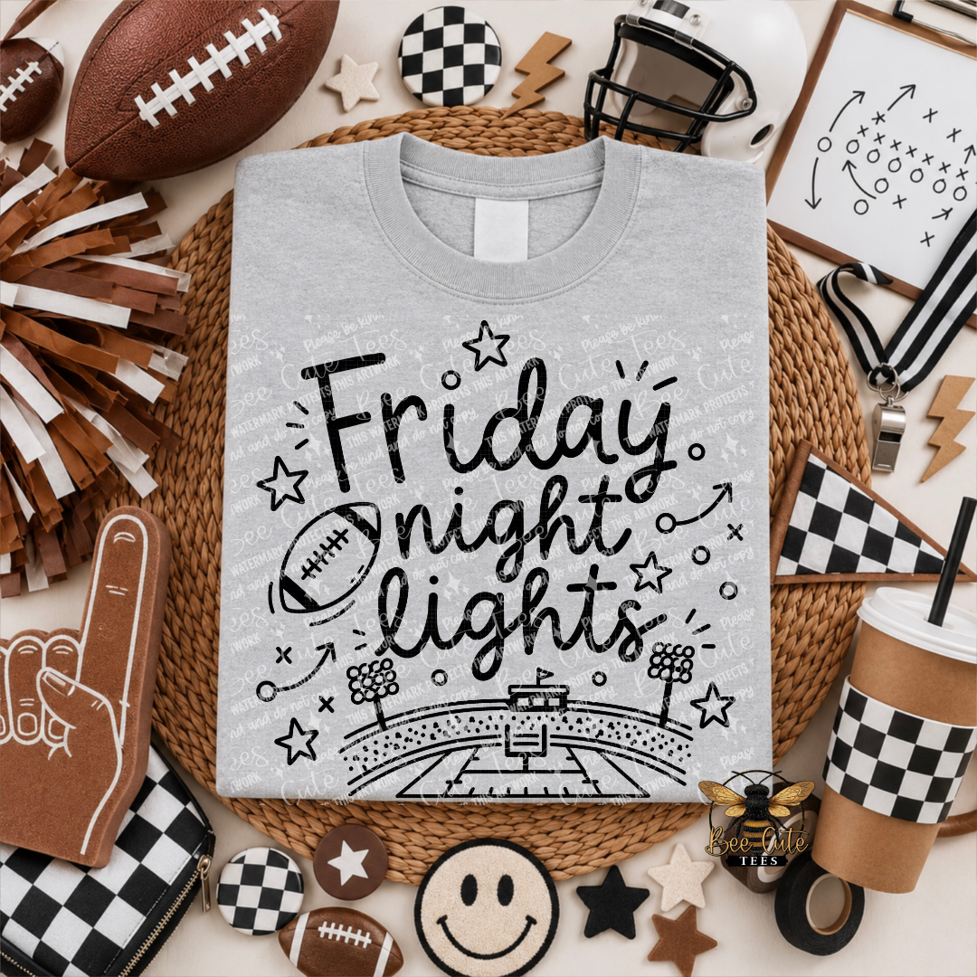 A light gray graphic t-shirt featuring the text 'Friday night lights' in black script with football and stadium illustrations, presented in a themed flat-lay with sports and party props.