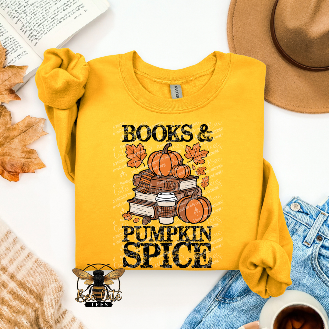 A folded yellow long-sleeve shirt with rolled sleeves, featuring a 'Books & Pumpkin Spice' graphic with pumpkins, autumn leaves, and books. The shirt is styled in a flat lay with a tan hat, blue jeans, a book, leaves, and a coffee cup on a white background.
