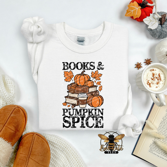 A white long-sleeve t-shirt with a 'BOOKS & PUMPKIN SPICE' graphic, styled in a cozy flat-lay arrangement with a mug of coffee, a book, knit socks, and autumn-themed decorations.