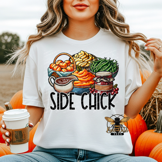 A woman wearing a white graphic t-shirt with a Thanksgiving-themed illustration and the text 'SIDE CHICK'. She is holding a coffee cup and surrounded by pumpkins.