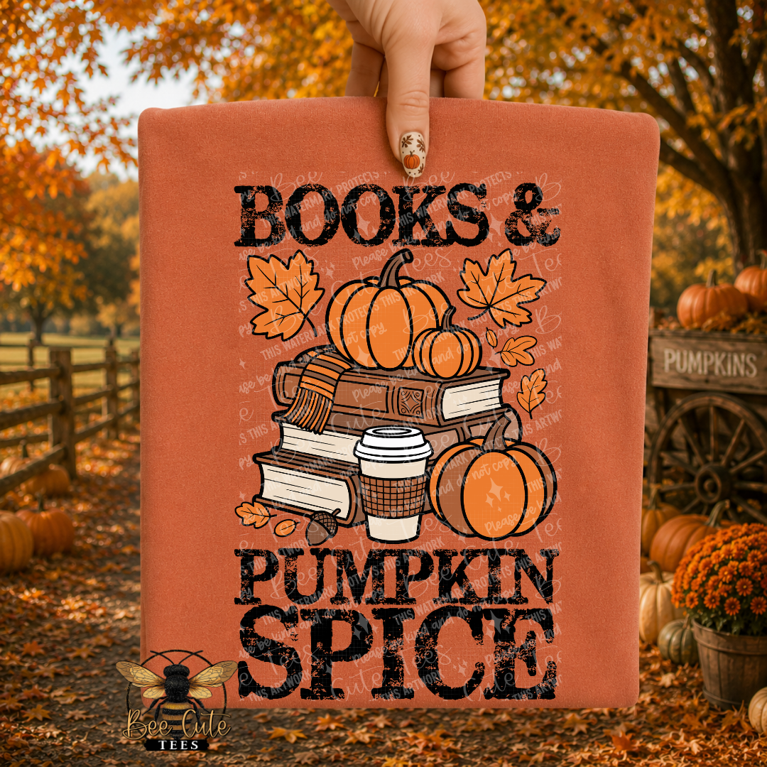 A hand holds up a folded terracotta-colored t-shirt featuring a 'Books & Pumpkin Spice' autumn graphic with pumpkins, books, and a coffee cup, set against an outdoor fall yard background.