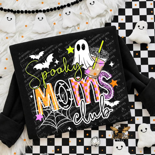 A black long-sleeve sweatshirt laid flat on a Halloween-themed background. The front has a large graphic reading 'Spooky Moms club' with a ghost, drink, bats, spiderwebs, stars, and orange/black patterned lettering.
