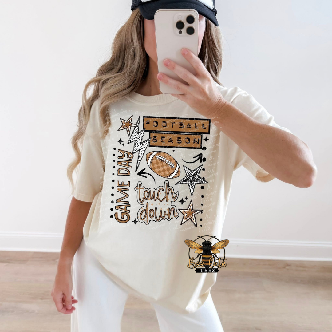 A woman takes a mirror selfie wearing a cream-colored graphic t-shirt with a 'Football Season Game Day Touchdown' design, paired with white pants and a black cap.
