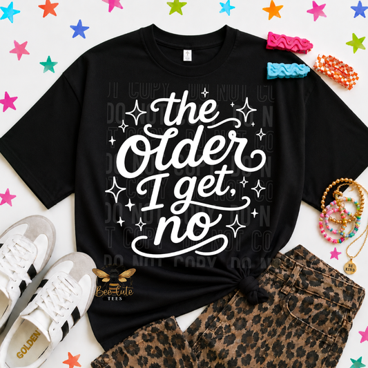 A black graphic T-shirt with the phrase 'the Older I get, no' in white script and sparkles, styled in a flat lay with leopard-print shorts, white sneakers, colorful scrunchies, bracelets, and star confetti on a white background.