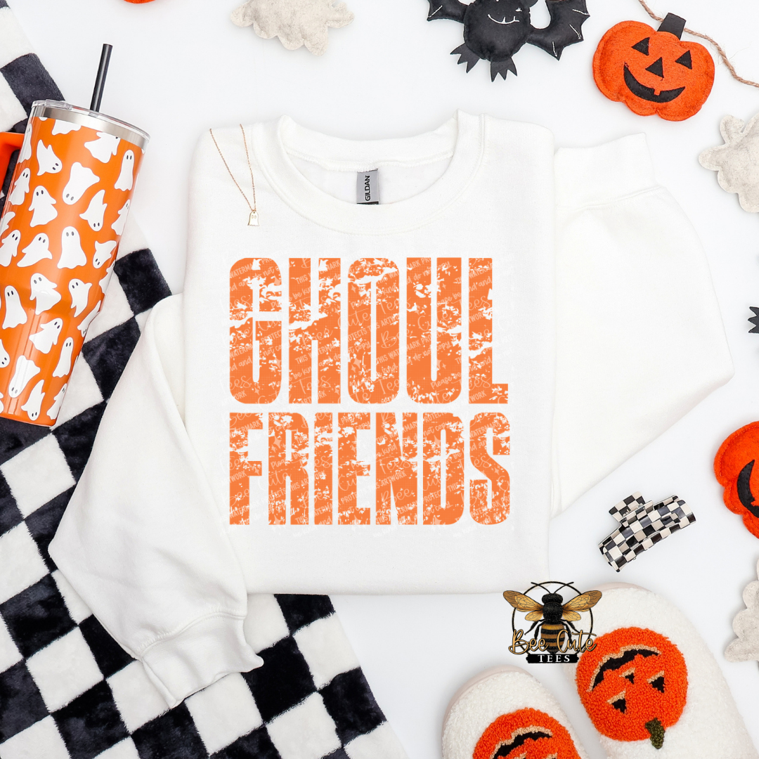 White crewneck sweatshirt featuring a distressed orange “Ghoul Friends” Halloween graphic, styled with an orange ghost tumbler, black-and-white checkered blanket, pumpkins, ghosts, and spooky seasonal accessories.