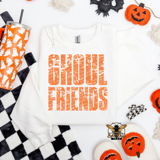 White crewneck sweatshirt featuring a distressed orange “Ghoul Friends” Halloween graphic, styled with an orange ghost tumbler, black-and-white checkered blanket, pumpkins, ghosts, and spooky seasonal accessories.