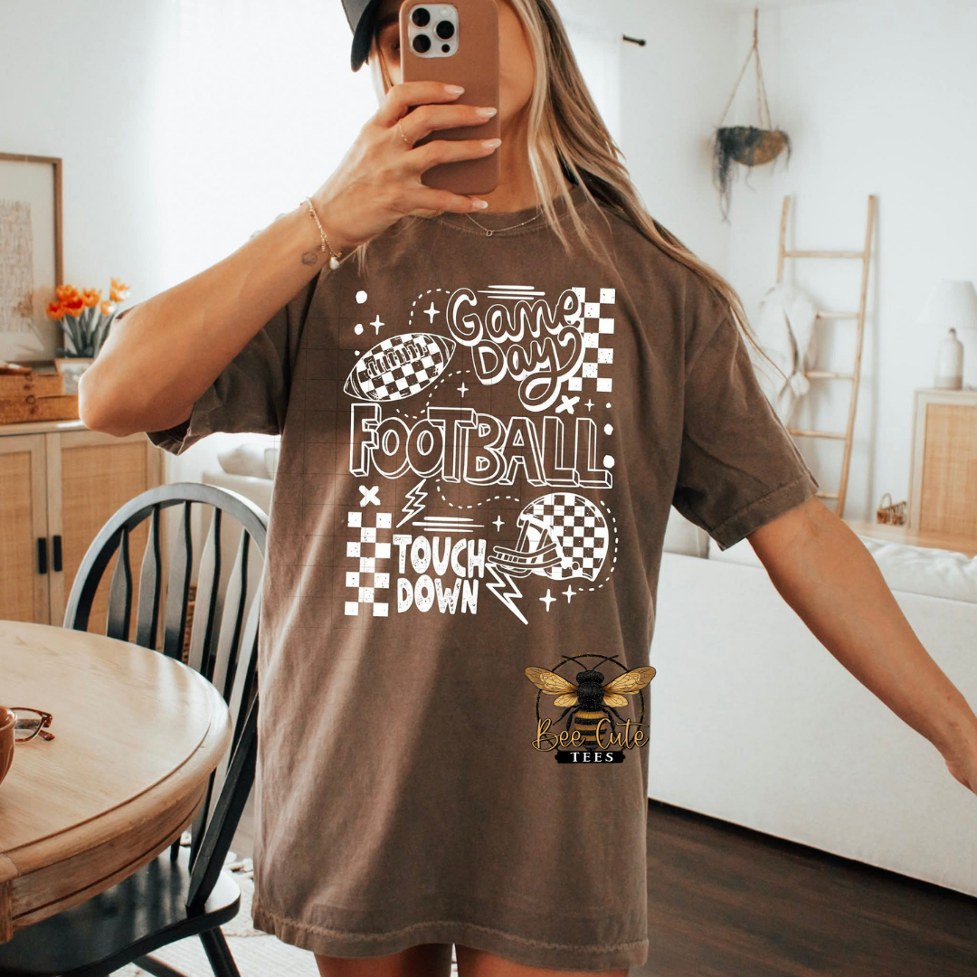 Person wearing a brown t-shirt with football-themed graphics in a home setting.