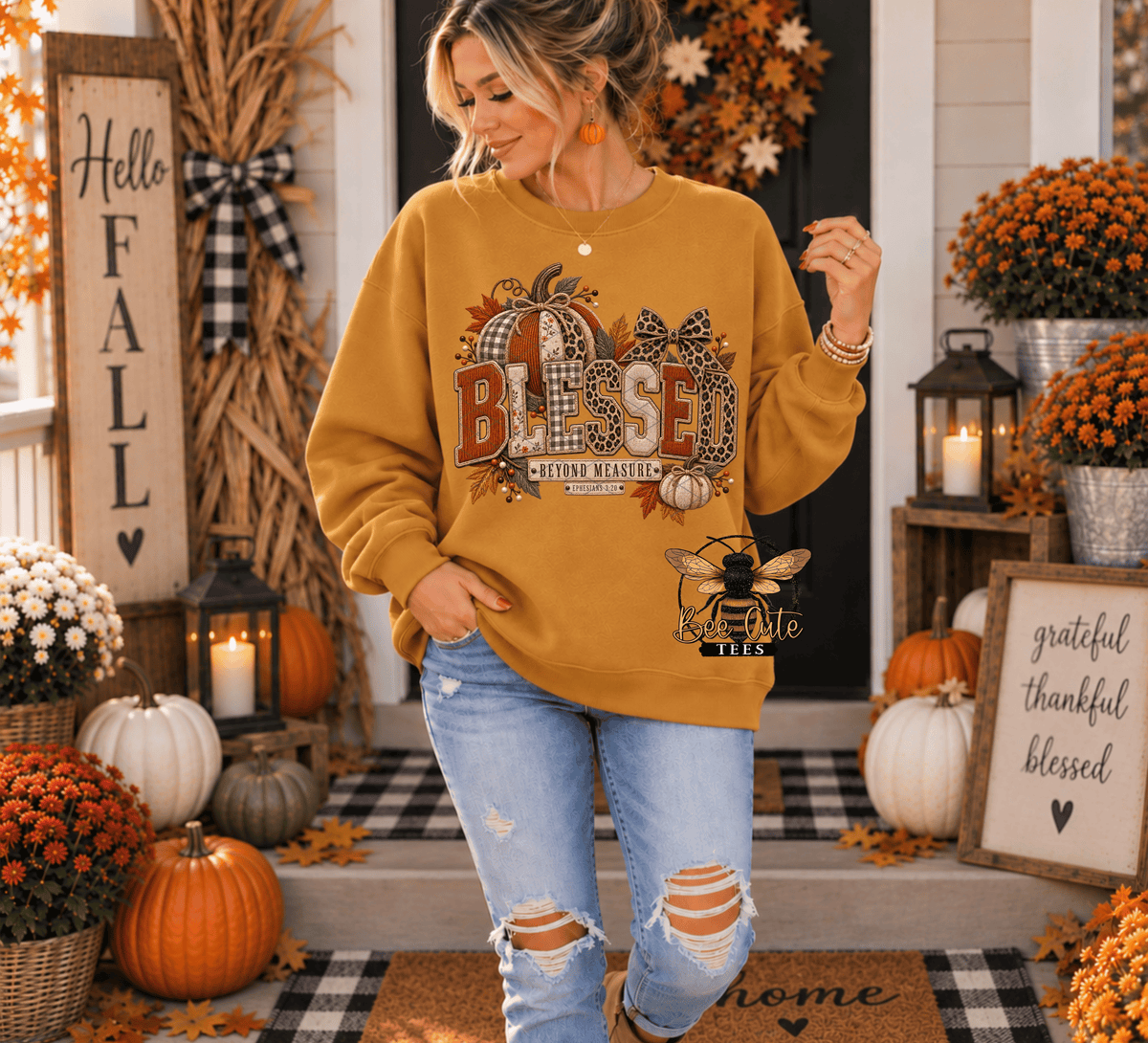 A woman modeling a mustard yellow crewneck sweatshirt with a large 'BLESSED' autumn graphic on the front, paired with distressed light blue jeans, standing on a decorated fall porch.