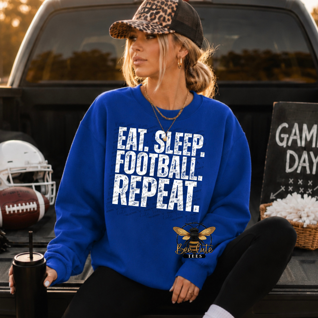 A woman sits in the bed of a pickup truck wearing a bright blue crewneck sweatshirt with the text 'EAT. SLEEP. FOOTBALL. REPEAT.'
