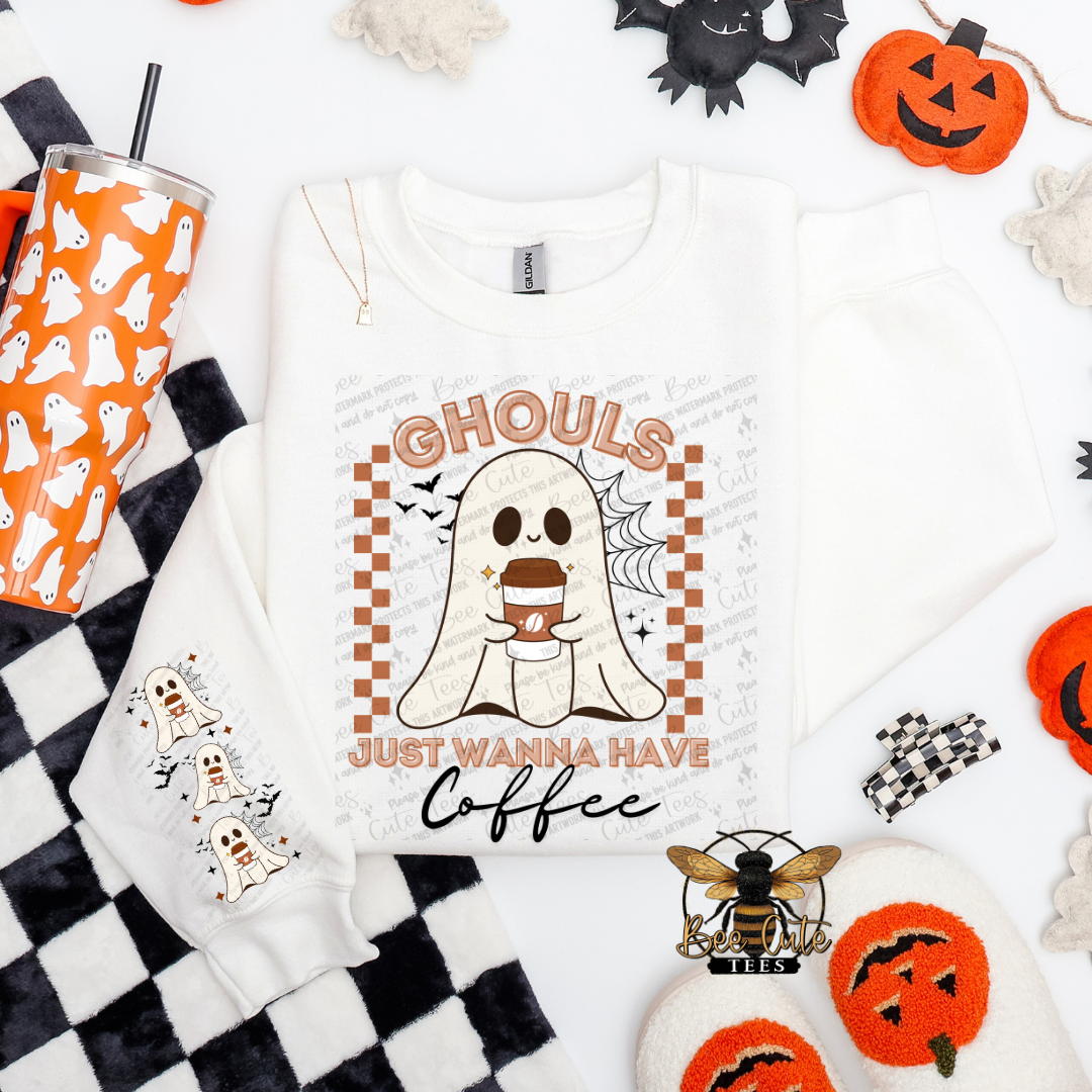 A white long-sleeve sweatshirt with a Halloween graphic print featuring a ghost holding a coffee cup and the text 'Ghouls Just Wanna Have Coffee'. The sweatshirt is styled in a flat-lay arrangement with a black and white checkered blanket, an orange and white ghost-patterned tumbler, black and white socks, and orange jack-o'-lantern decorations on a white background.