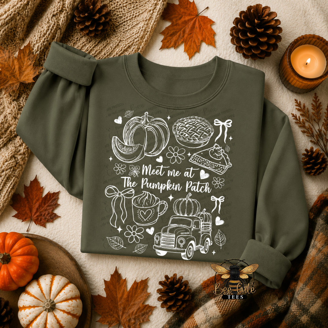 An olive green long-sleeve sweatshirt with a white autumn-themed graphic print reading 'Meet me at The Pumpkin Patch' and illustrations of pumpkins, a pie, a truck, and bows, styled in a flat lay with fall leaves, pinecones, a candle, and a knit blanket.