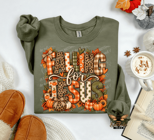 An olive green long-sleeve t-shirt with a 'FALLING FOR JESUS' autumn-themed graphic, styled in a cozy flat-lay arrangement with a mug of coffee, an open book, and brown slippers.