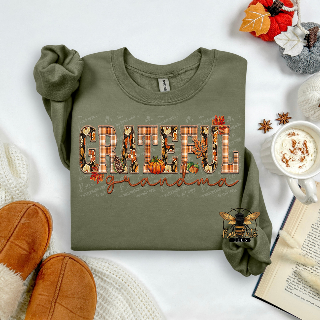 An olive green long-sleeve t-shirt with a 'GRATEFUL grandma' graphic in autumn-themed letters, styled in a cozy flat-lay with a mug of coffee, an open book, and brown suede shoes.